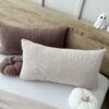 Poduszka z miękkiej dzianiny boucle w ciepłym brązie, ułożona u góry łóżka, prezentująca elegancki i przytulny wygląd sypialni